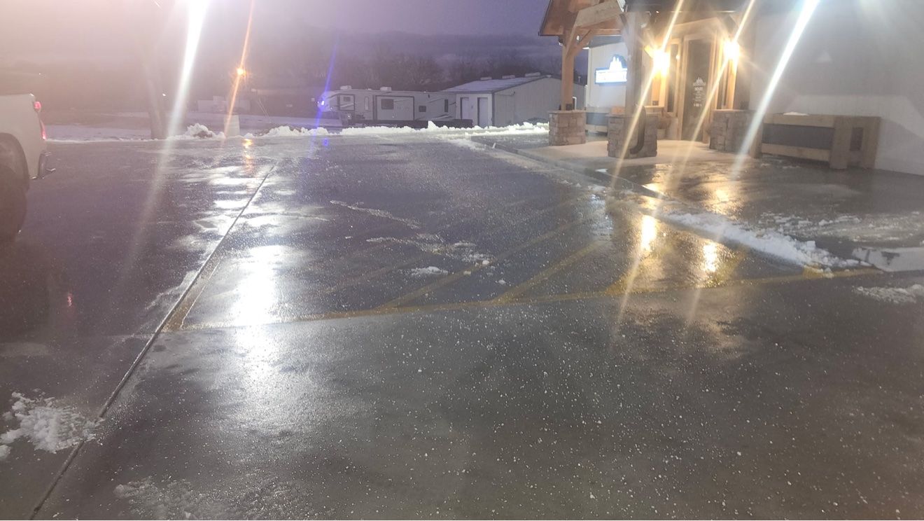 Cleared commercial parking lot at night with wet pavement reflecting bright building lights