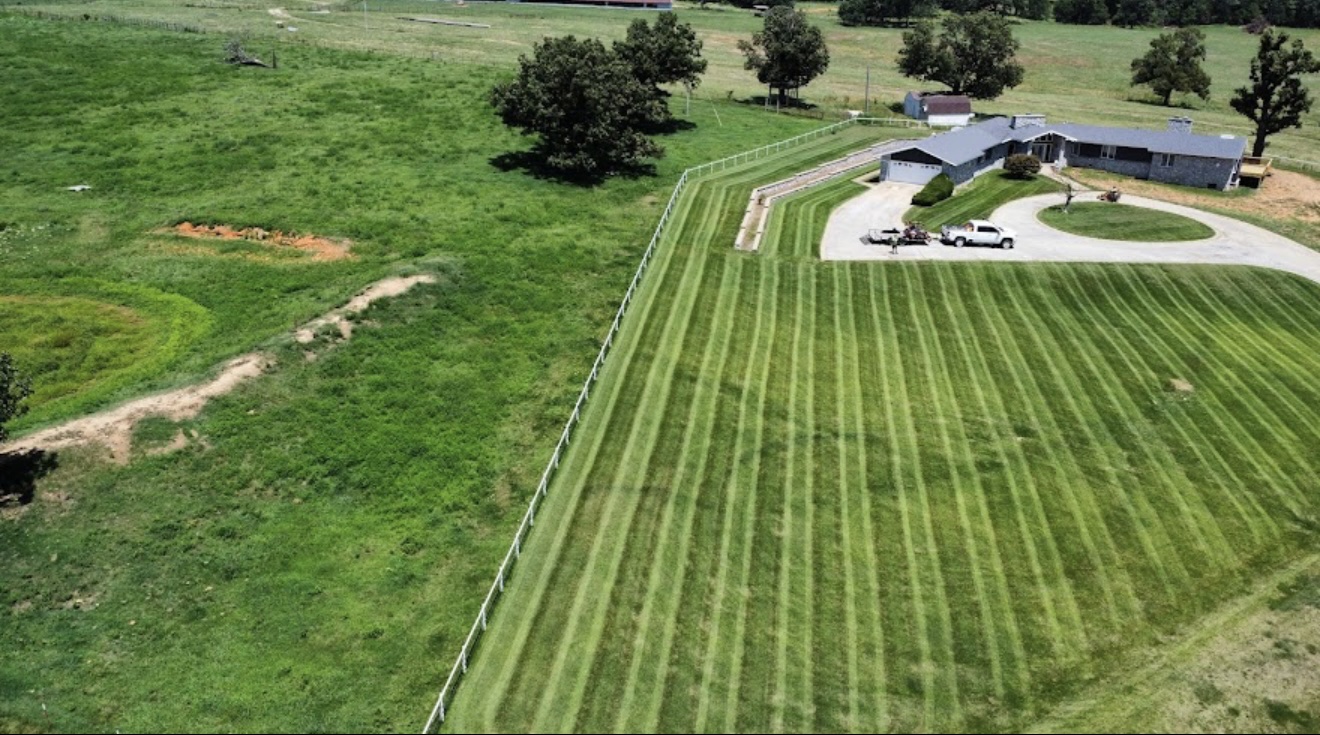 Aerial view of a large country lawn cut with crisp alternating mowing stripes next to a house and white fence